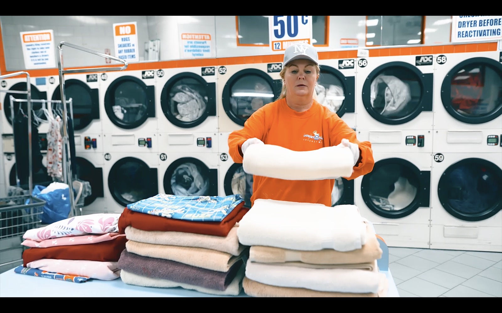 A Laundry King team member in an orange uniform folding fresh towels in the Brooklyn shop
